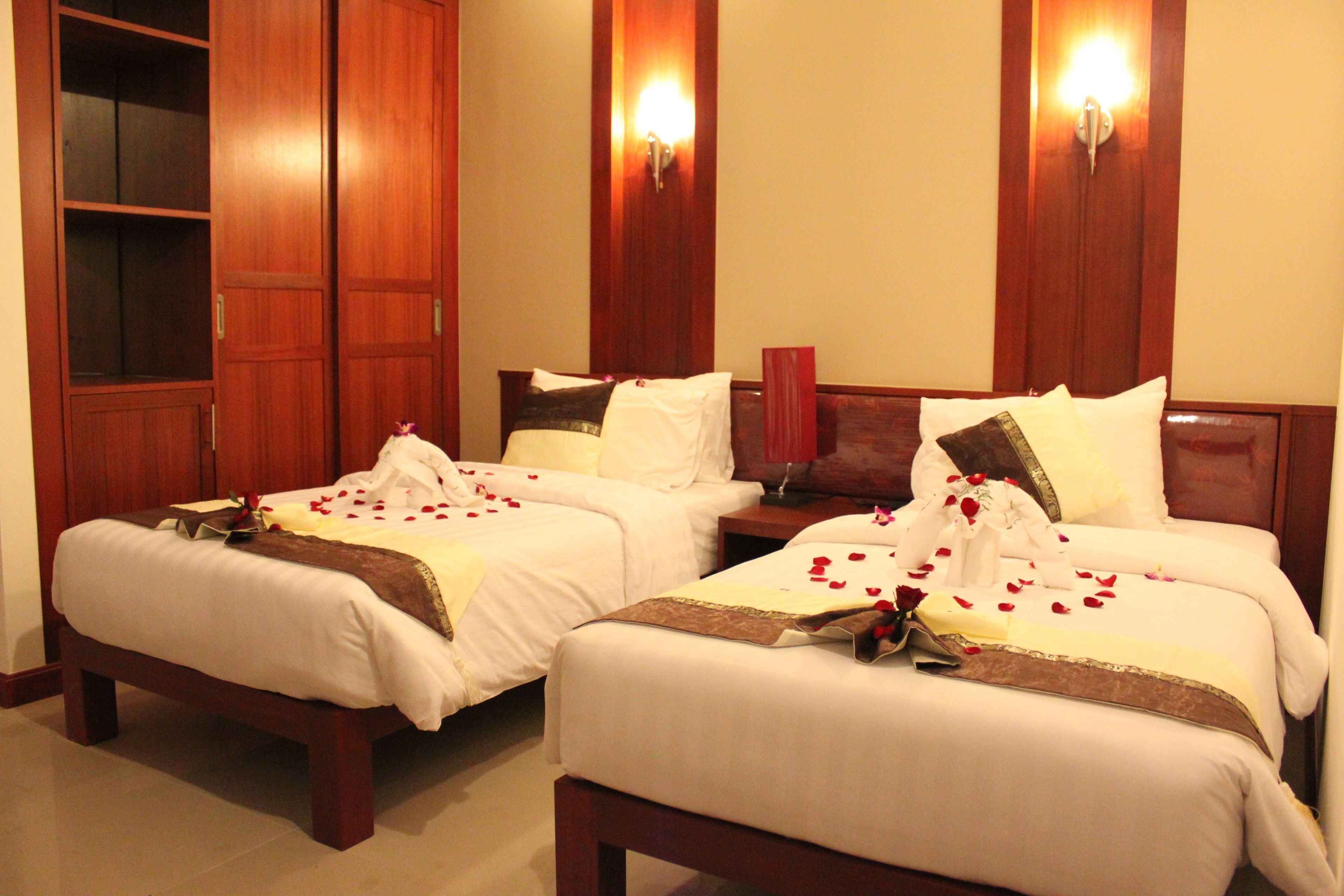 A hotel room with two beds, wooden headboards, and wall-mounted light fixtures.