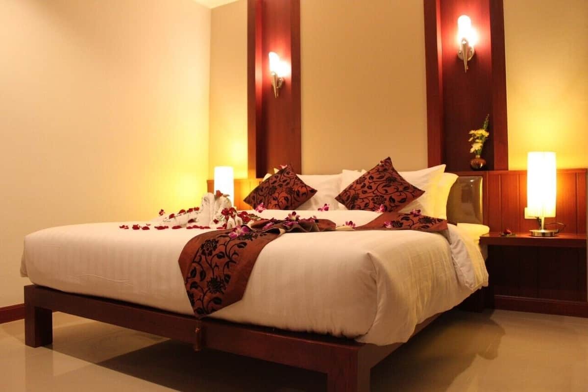 A neatly made bed with a white and brown bedspread, two decorative pillows, and a floral arrangement on the nightstand.