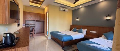 A hotel room with two beds, a wooden wardrobe, a kitchenette, and a ceiling fan.