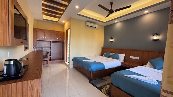 A hotel room with two beds, a wooden wardrobe, a kitchenette, and a ceiling fan.