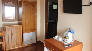 A hotel room with a wooden wardrobe, a desk with a tray of toiletries, a remote control, and a flat-screen TV mounted on the wall. - Jungle Wildlife Camp (Sauraha)