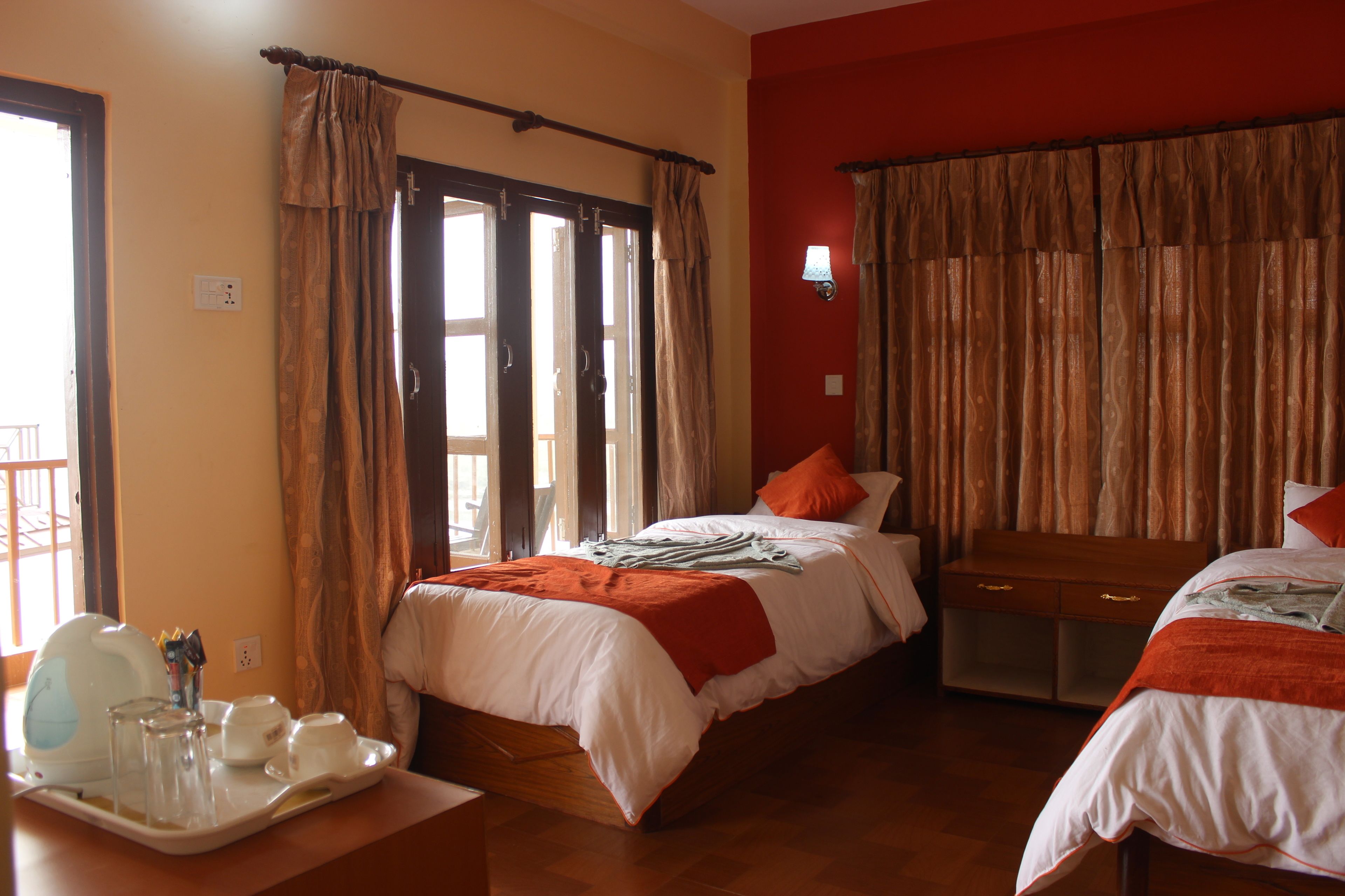 Une chambre d’hôtel avec un lit, une table de chevet sur laquelle se trouve un plateau avec divers objets, une fenêtre avec des rideaux et une table de nuit en bois.