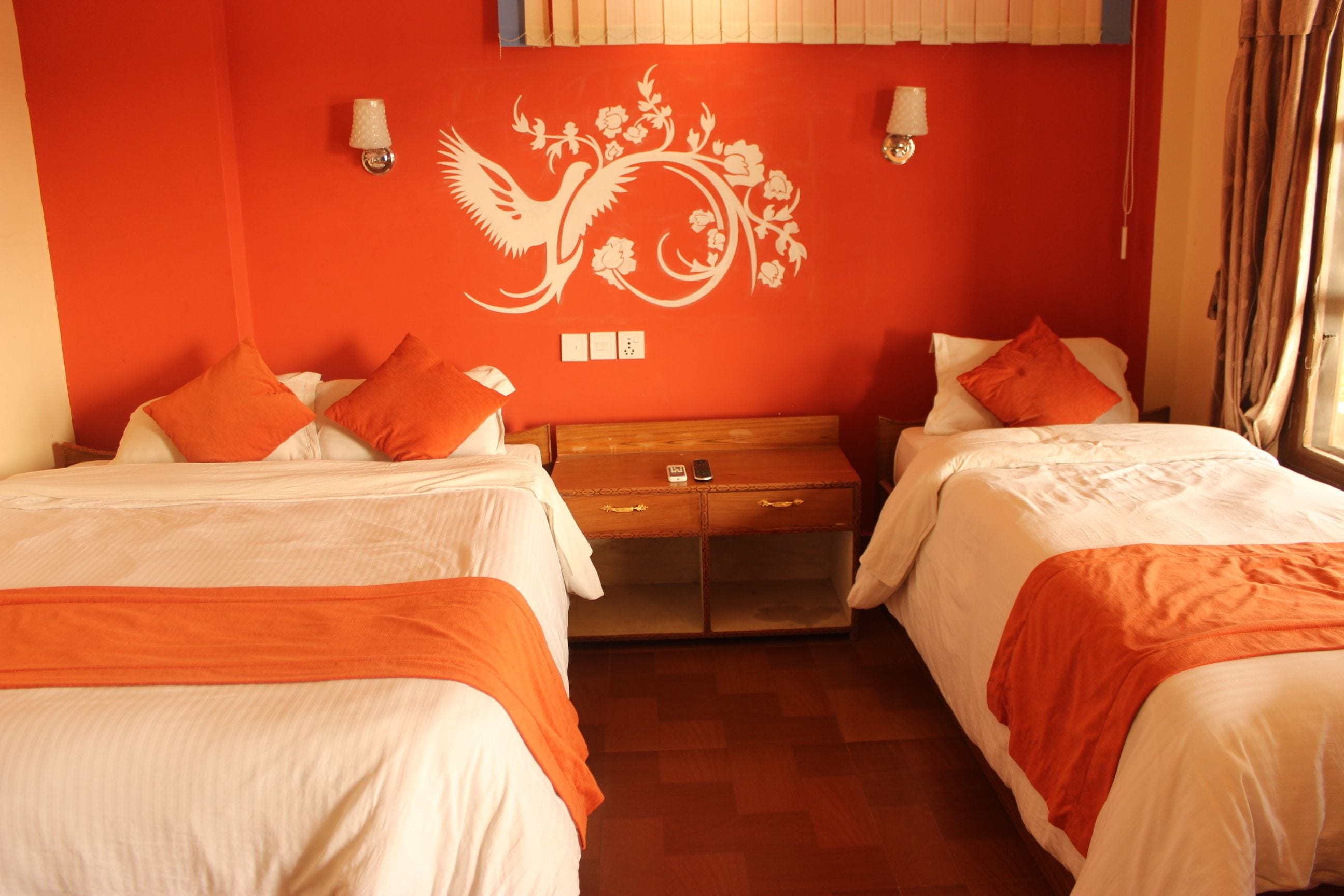 A hotel room with two beds, a wooden chest of drawers, and a decorative wall mural.