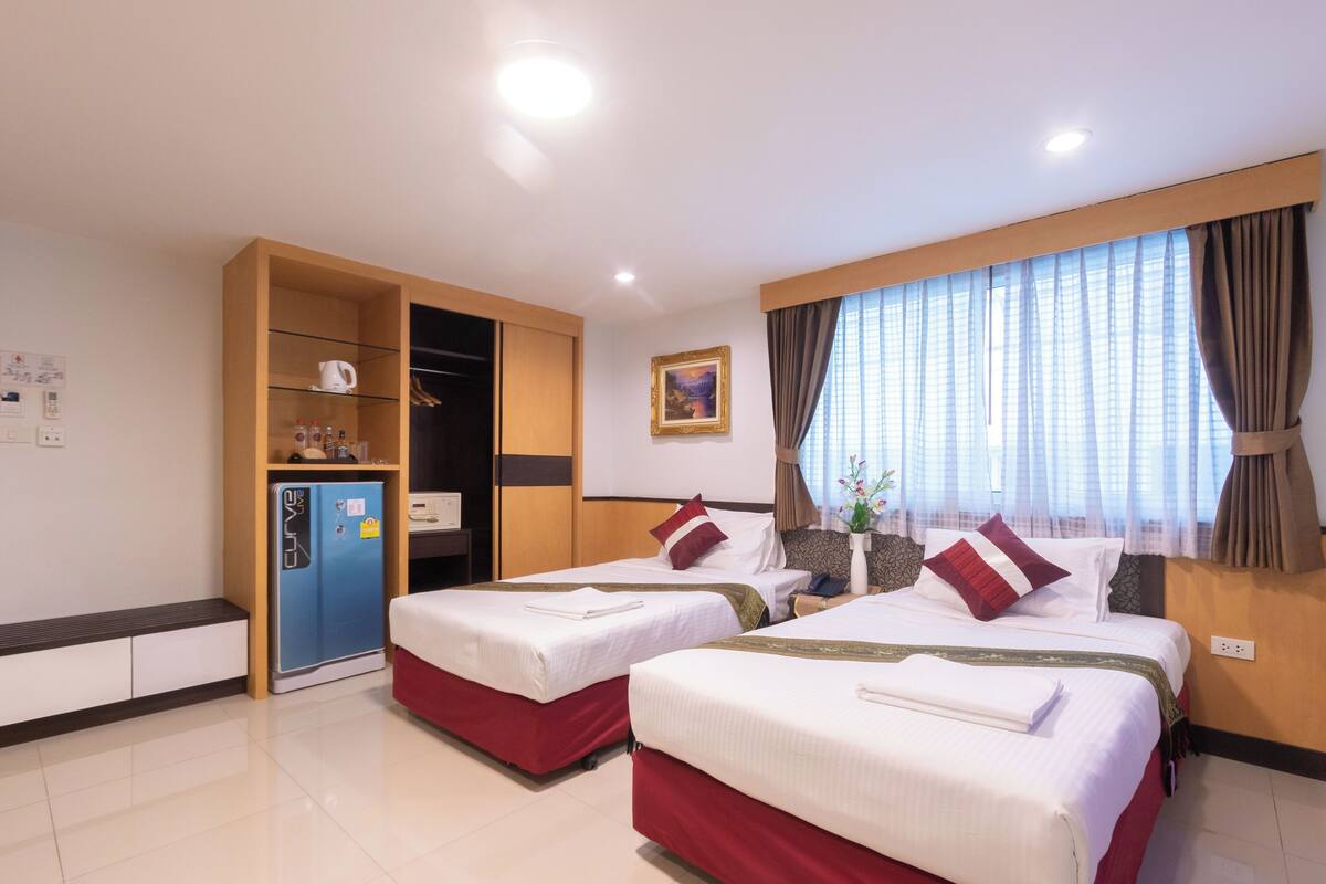 A hotel room with two beds, a wardrobe, a minibar, and a window with curtains.