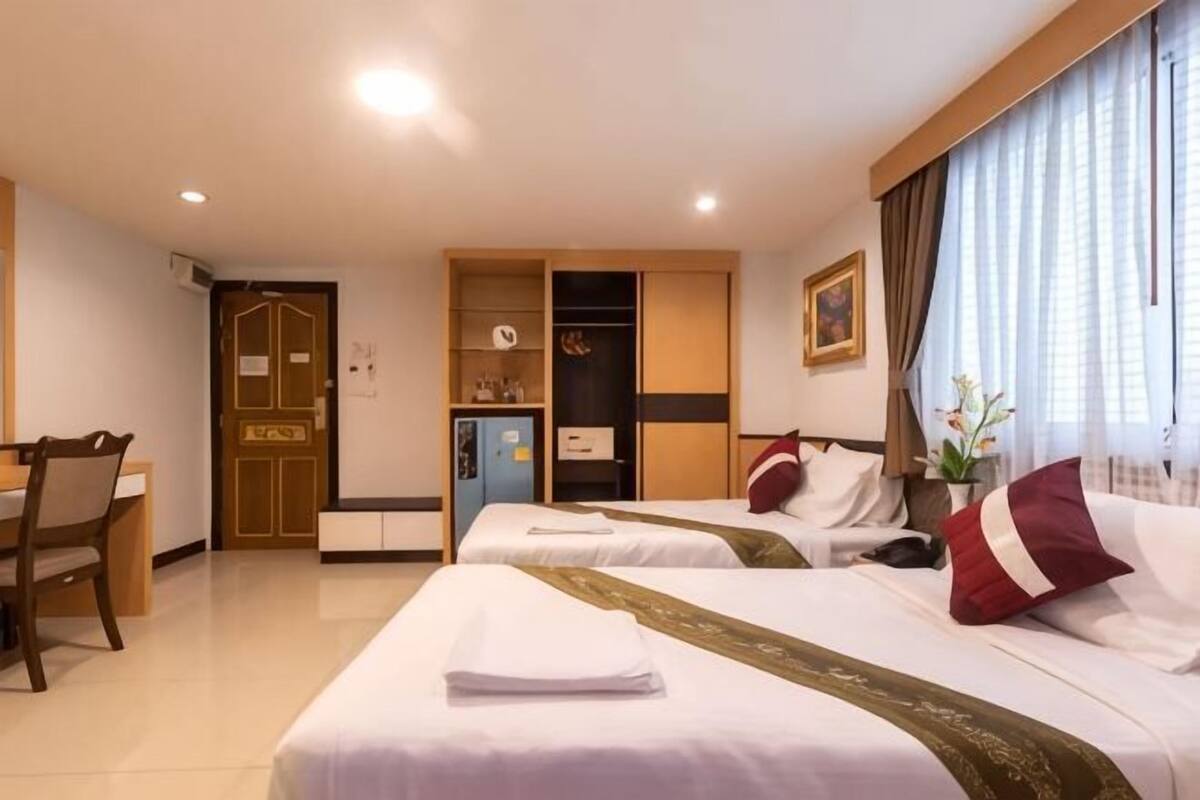 A hotel room with two beds, a desk, a wardrobe, and a small kitchenette.