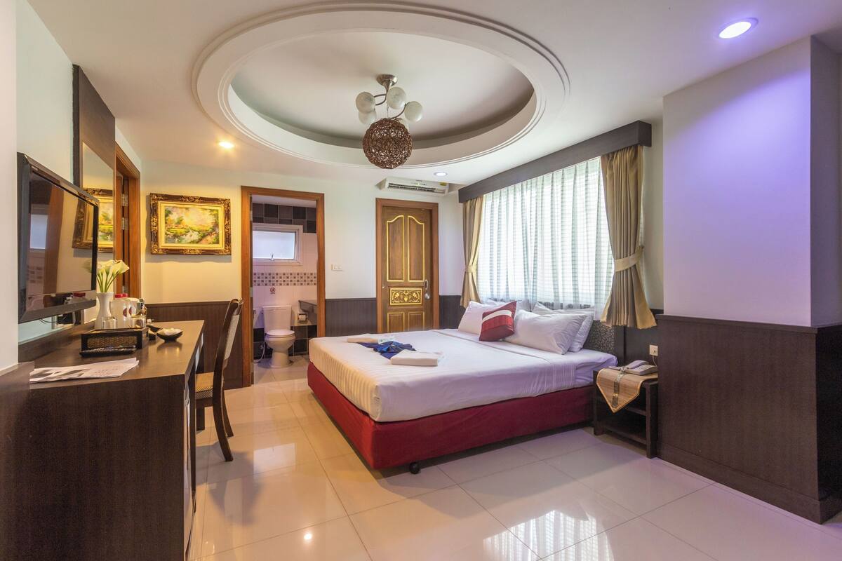 A hotel room with a bed, desk, chair, and a ceiling light fixture.