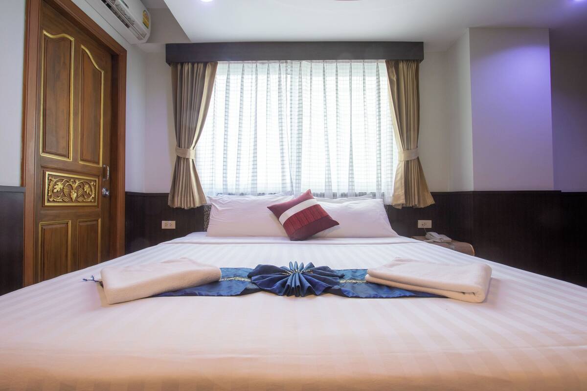 A hotel room with a neatly made bed, a wooden door, and a window with curtains.