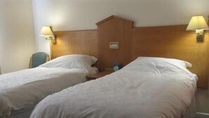 Een hotelkamer met twee eenpersoonsbedden, een houten hoofdbord en twee wandlampen.