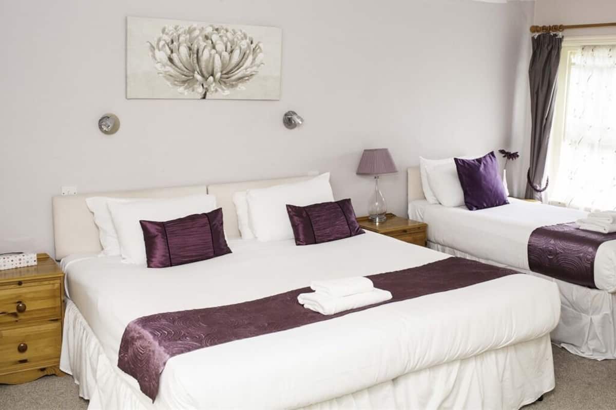 A hotel room with two beds, a nightstand, a lamp, and a window with curtains.