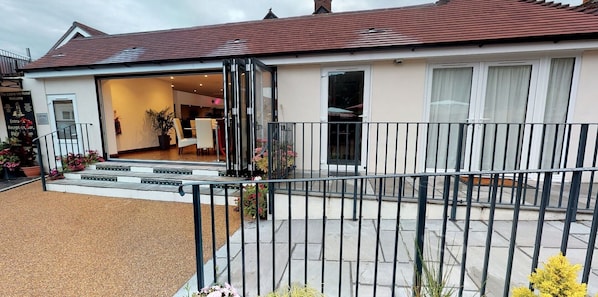 A hotel entrance with a reception desk, a staircase leading to the entrance, and a fenced outdoor area with potted plants.