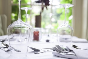 A table set with clear wine glasses, forks, and spoons, with a blurred green background. - The Castle Inn Hotel (Steyning)