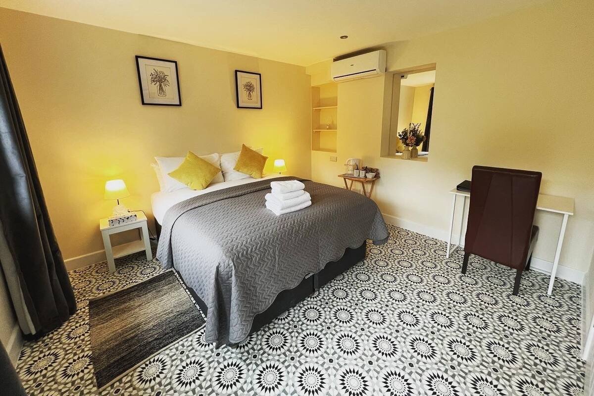 A hotel room with a bed, bedside tables, a mirror, a wardrobe, and patterned floor tiles.