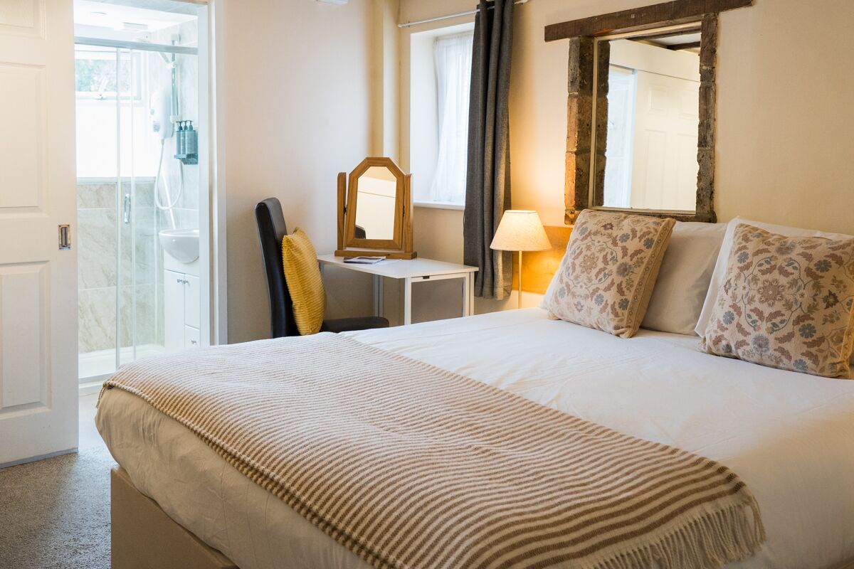 Hotelkamer met een bed, nachtkastje, spiegel, lamp en douchegedeelte.