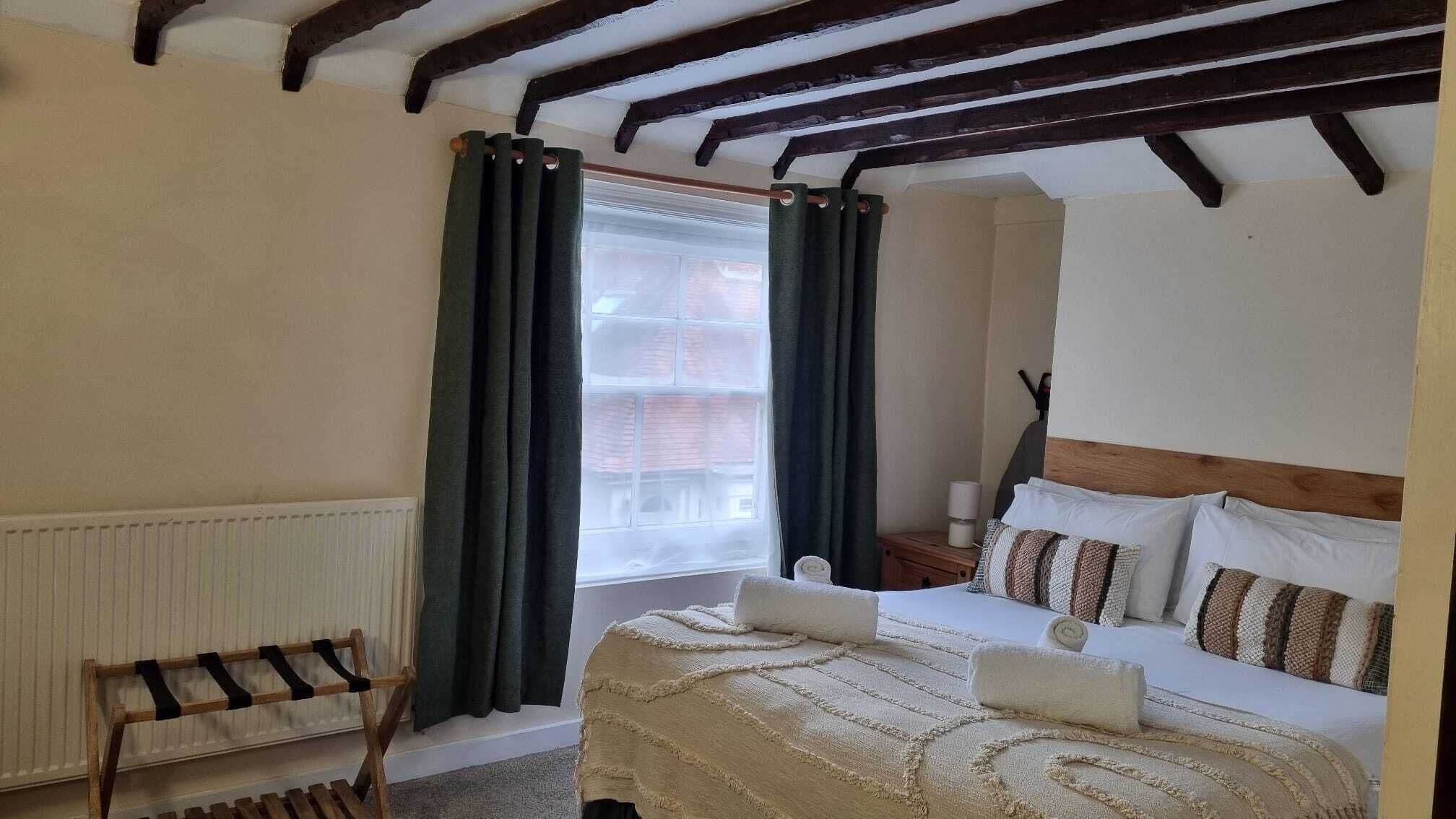 Un dormitorio acogedor con cama, mesita de noche, silla de madera y ventana con cortinas.