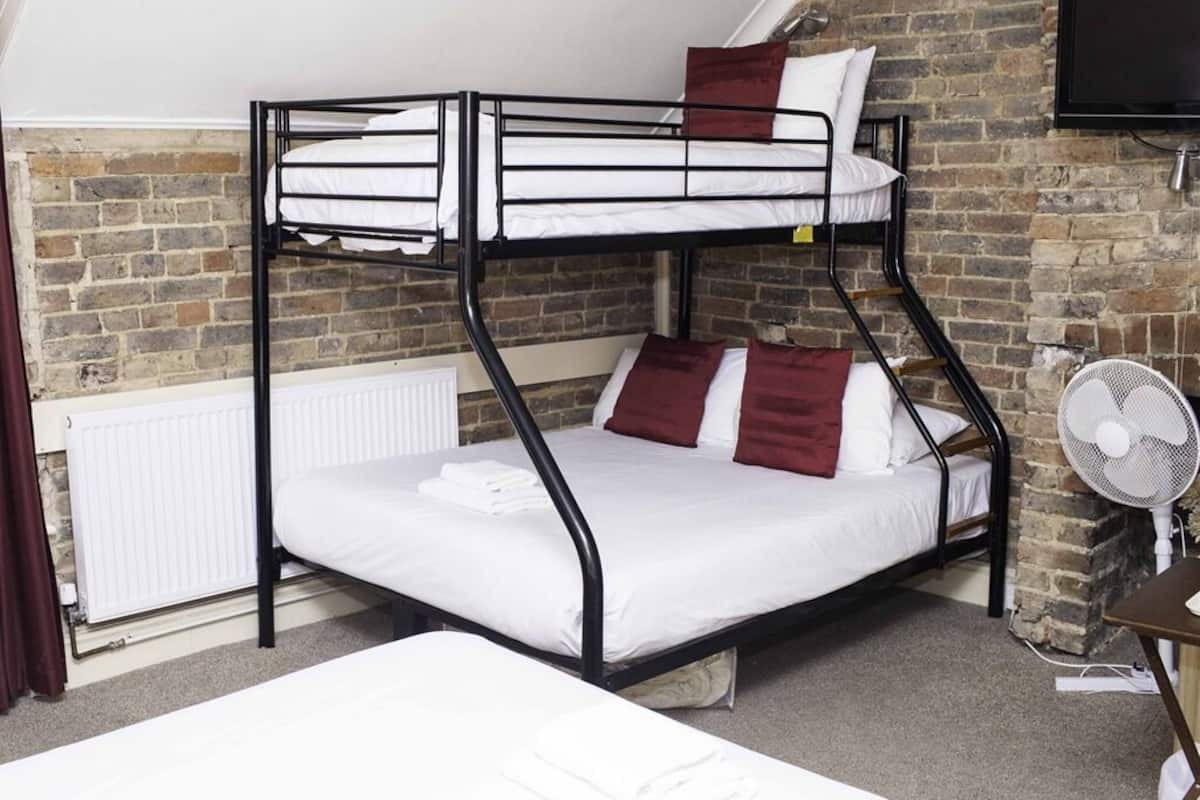 A bunk bed room with a brick wall, a radiator, and a fan.
