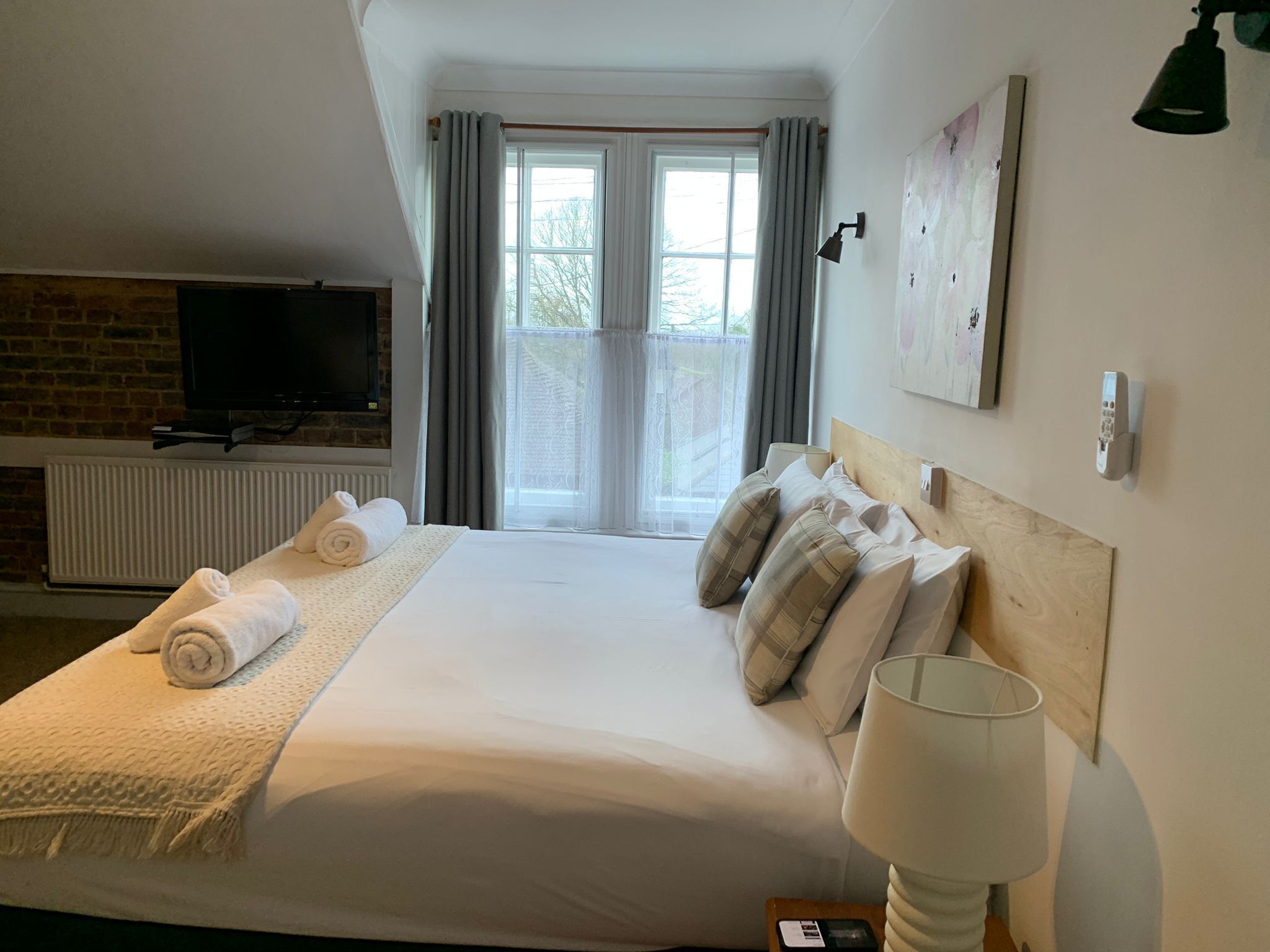 Una habitación de hotel con cama, televisión, chimenea, ventana con cortinas y lámpara.