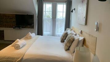 Una habitación de hotel con cama, televisión, chimenea, ventana con cortinas y lámpara.