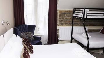 A hotel room with a bed, a chair, a window with curtains, and a bunk bed.