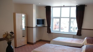 Habitación de hotel con dos camas, televisor, armario y ventana con cortinas.