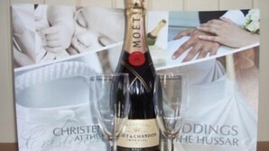 Una botella de Moët & Chandon champagne con dos copas sobre una mesa, con imágenes con temática nupcial de fondo.