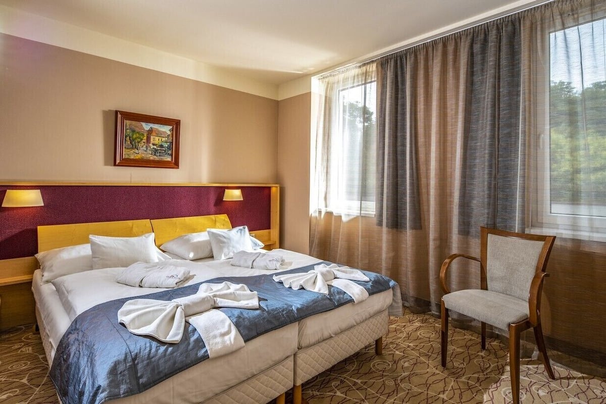 Ein Hotelzimmer mit einem großen Bett, zwei Nachttischlampen, einem Sessel und einem Bild an der Wand.
