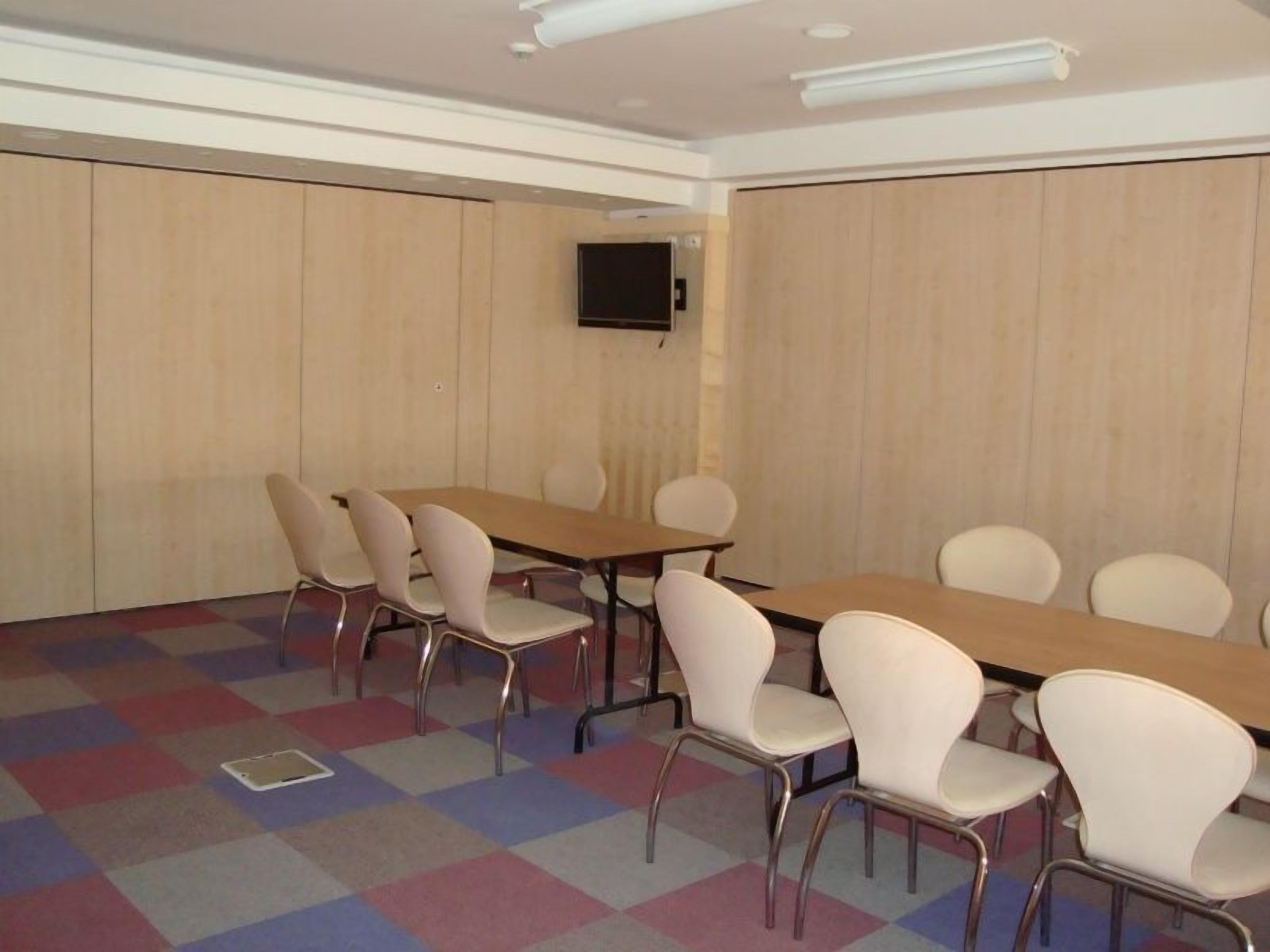 A conference room with a large table and chairs, a flat-screen TV mounted on the wall, and a patterned carpet.