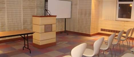 Un salón de conferencias con una pizarra, un atril y filas de sillas.