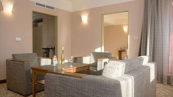 Una habitación de hotel con una mesa de comedor, cuatro sillones, un sofá, un minibar y un espejo grande.