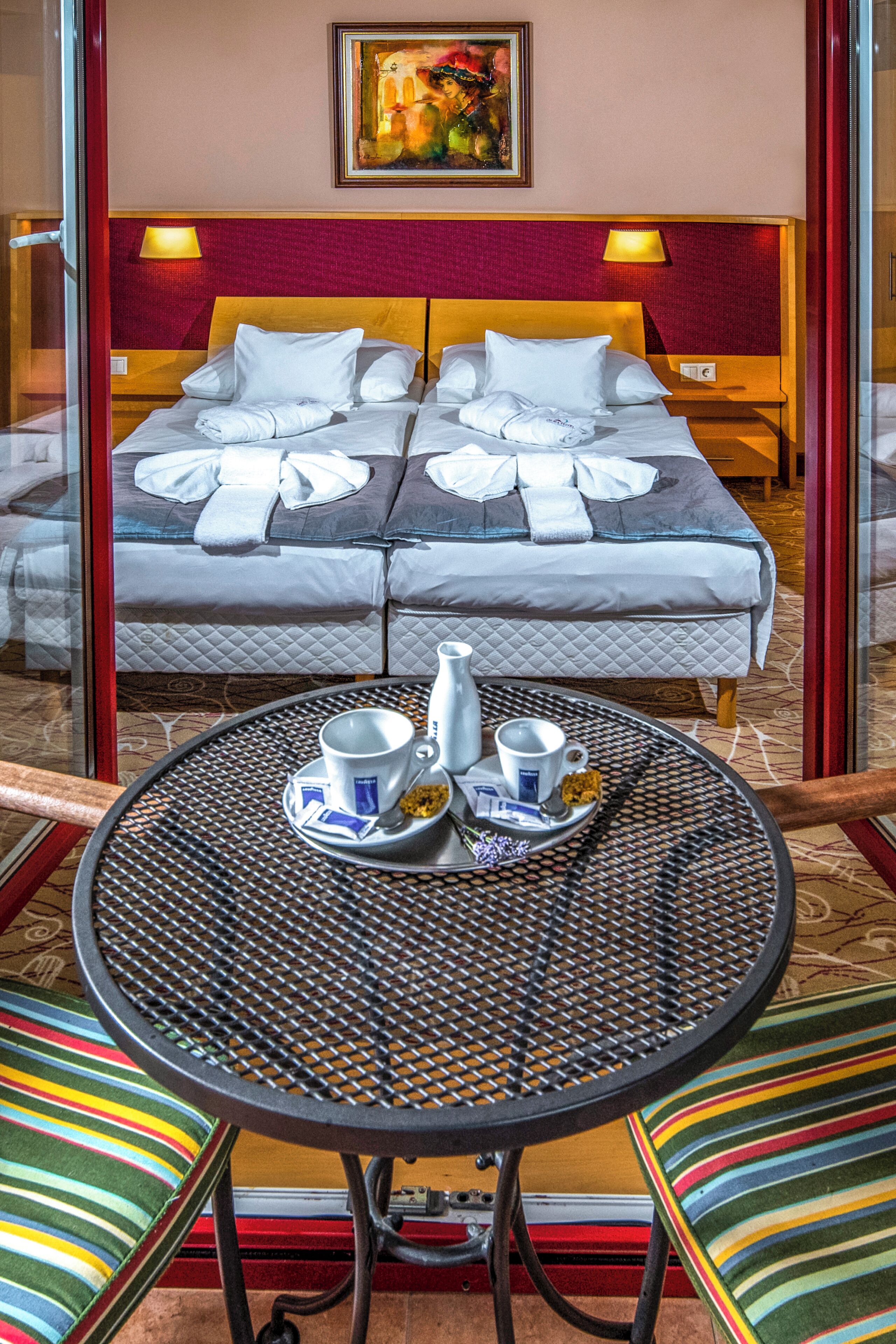 A hotel room with two beds, a dining table with breakfast items, and a painting on the wall.