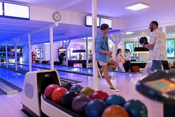 Une salle de bowling avec plusieurs pistes, une horloge au mur et des gens qui jouent.