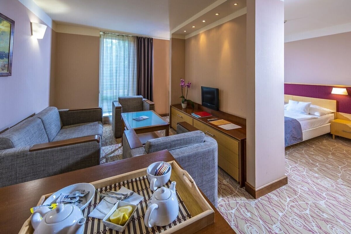 Ein Hotelzimmer mit einer Couch, einem Esstisch mit Frühstück und einem Fernseher sowie einem Bett.