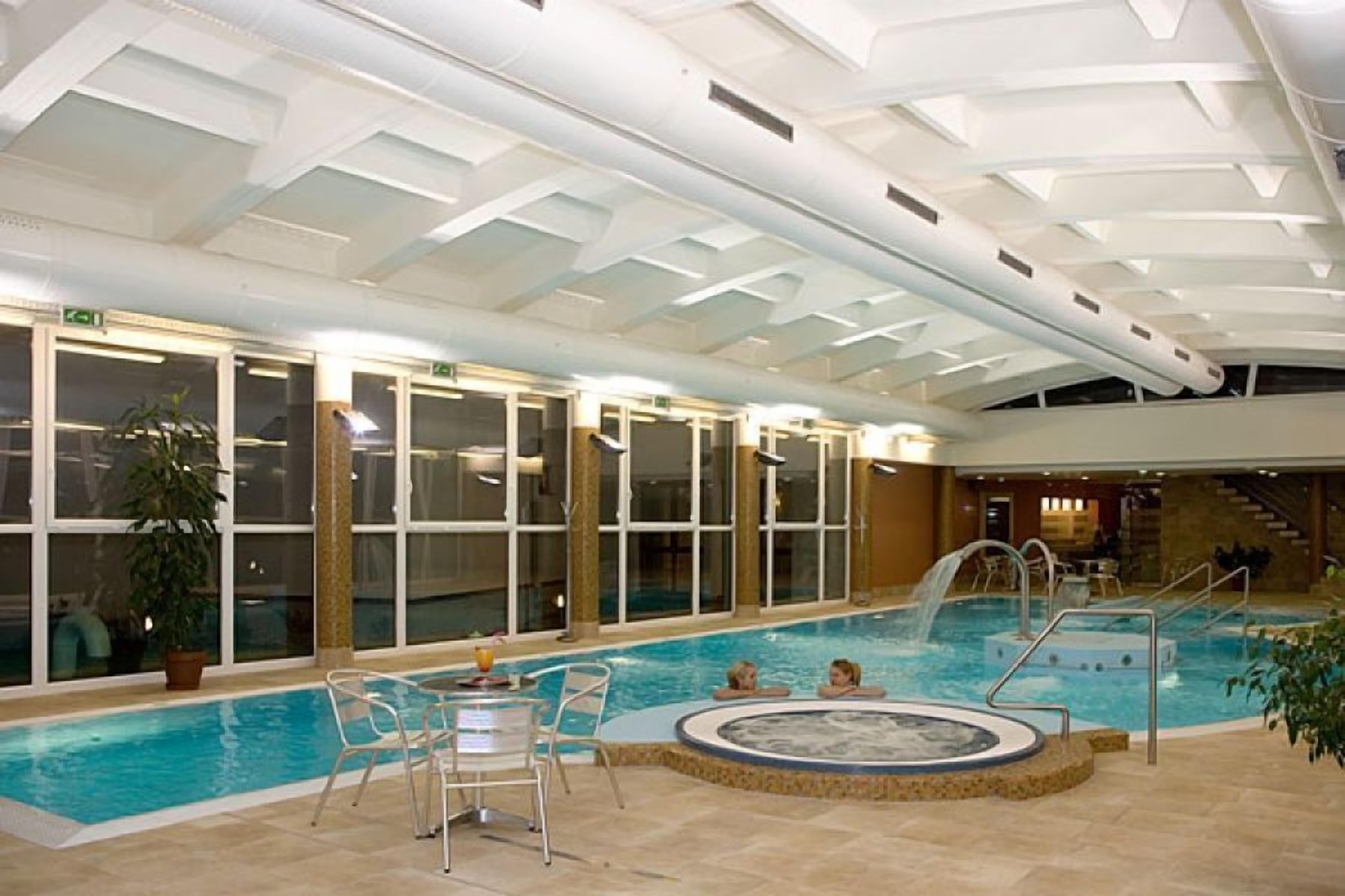 An indoor swimming pool with clear glass walls, a hot tub, and a staircase leading to an upper level.