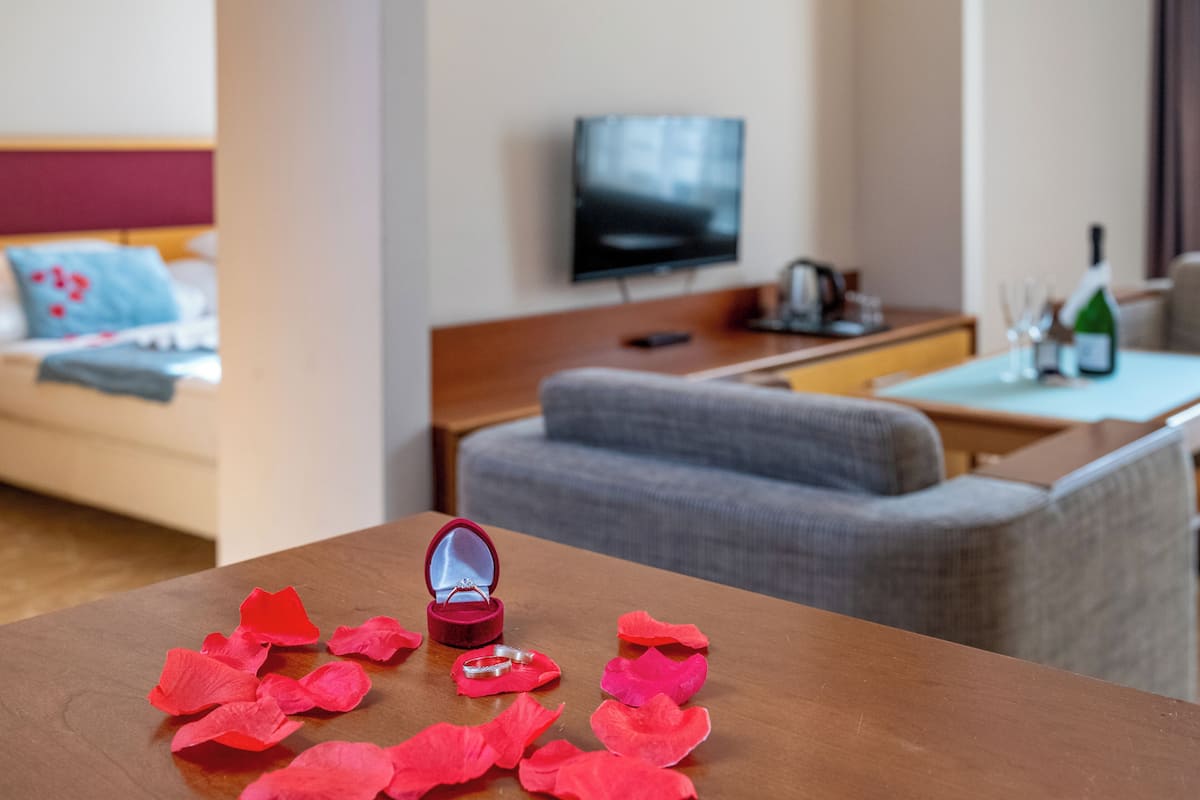 Ein Holztisch mit einer Ringbox und Rosenblüten, ein Fernseher und ein Sofa in einem modernen Wohnzimmer.