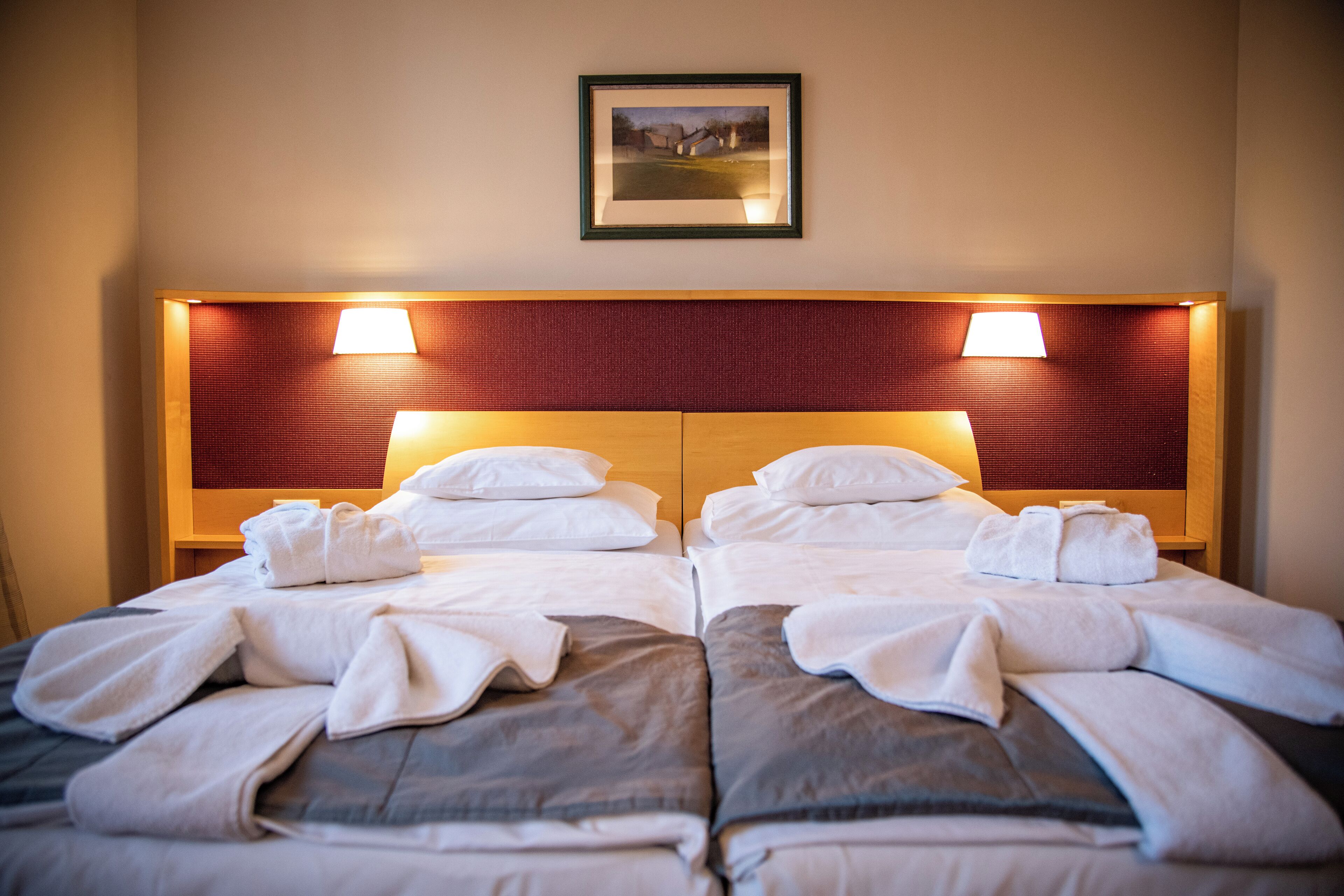 Cama doble con ropa y toallas blancas, cabecera de madera y dos lámparas de pared.