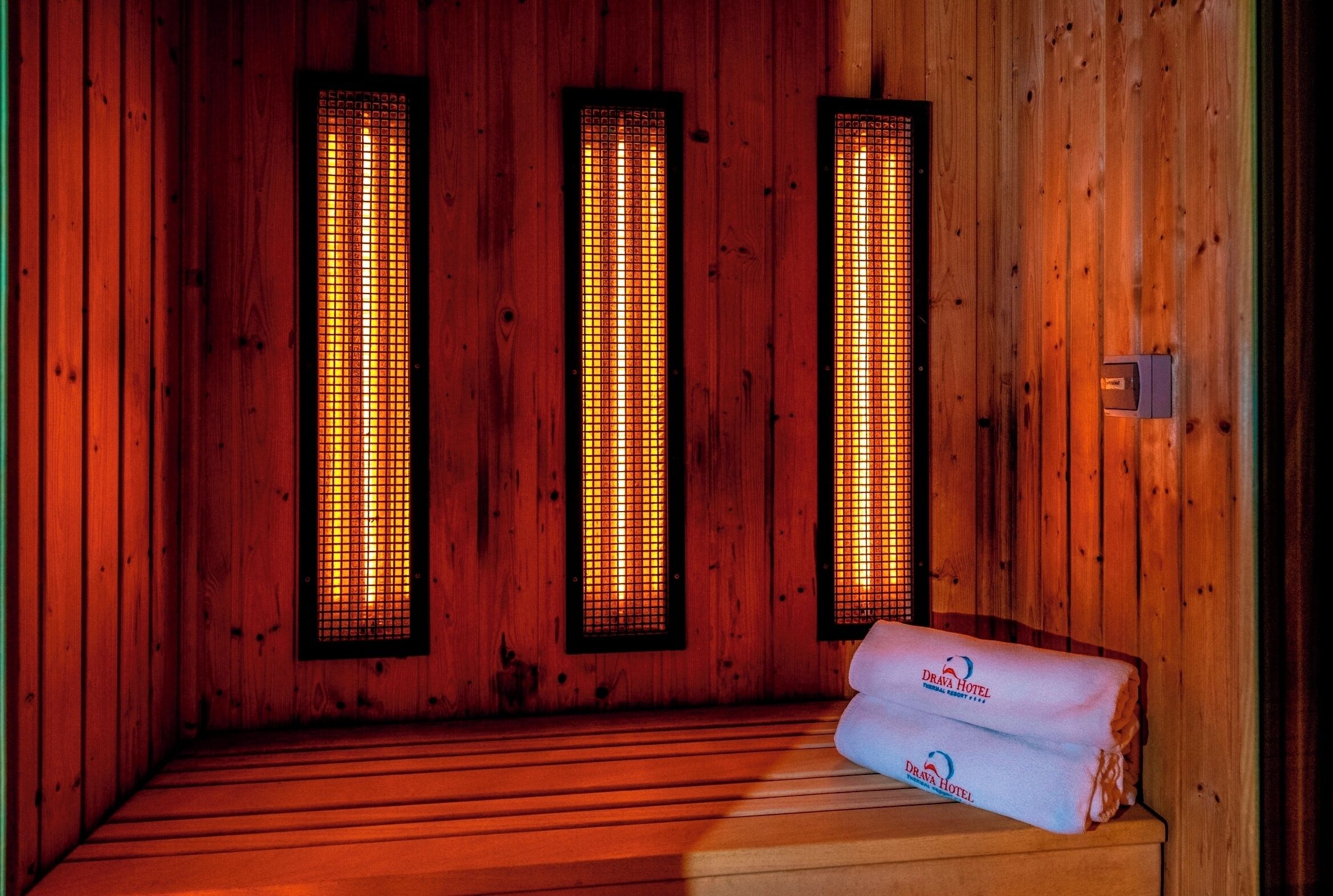 Een sauna met houten wanden en banken, met daarin drie infraroodpaneel verwarming en een handdoek op een bank.