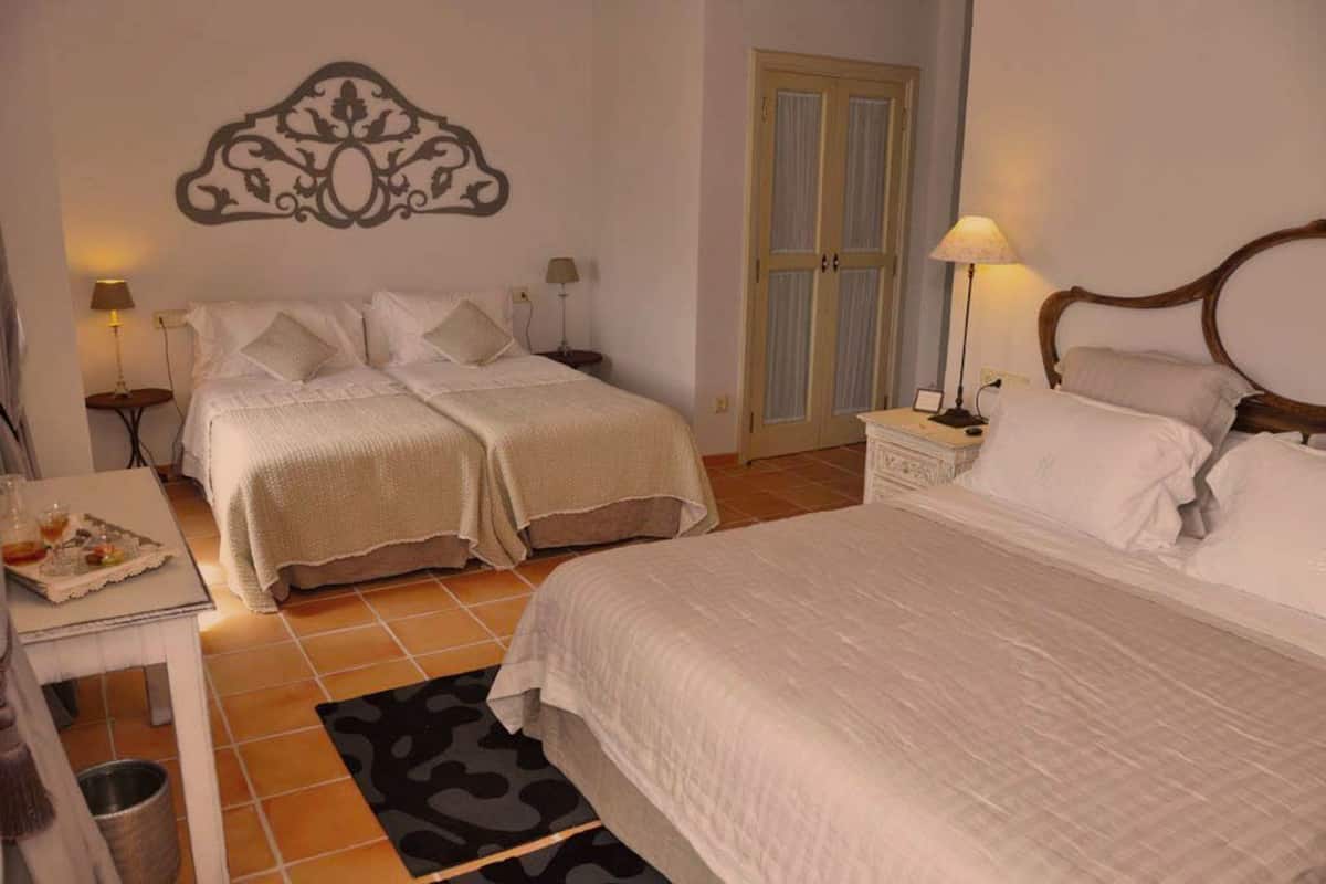 A hotel room with two beds, a small table with a tray of snacks, a lamp, and a decorative wall piece.