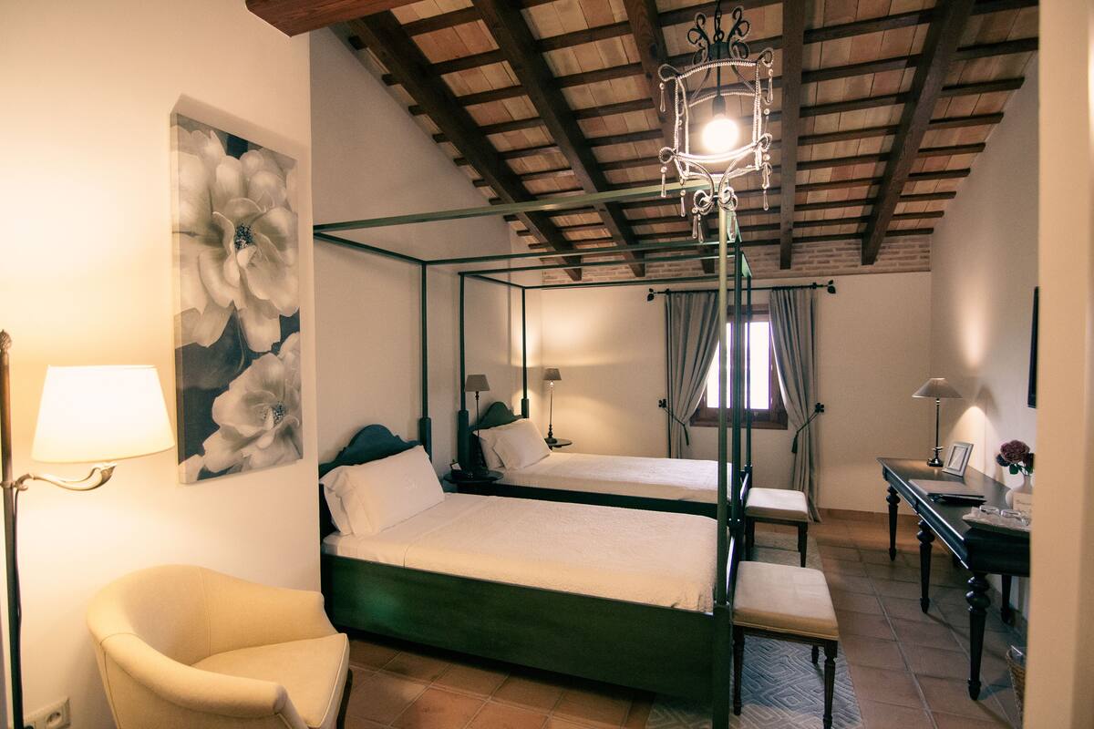 A bedroom with two beds, a chair, a desk, and a chandelier.