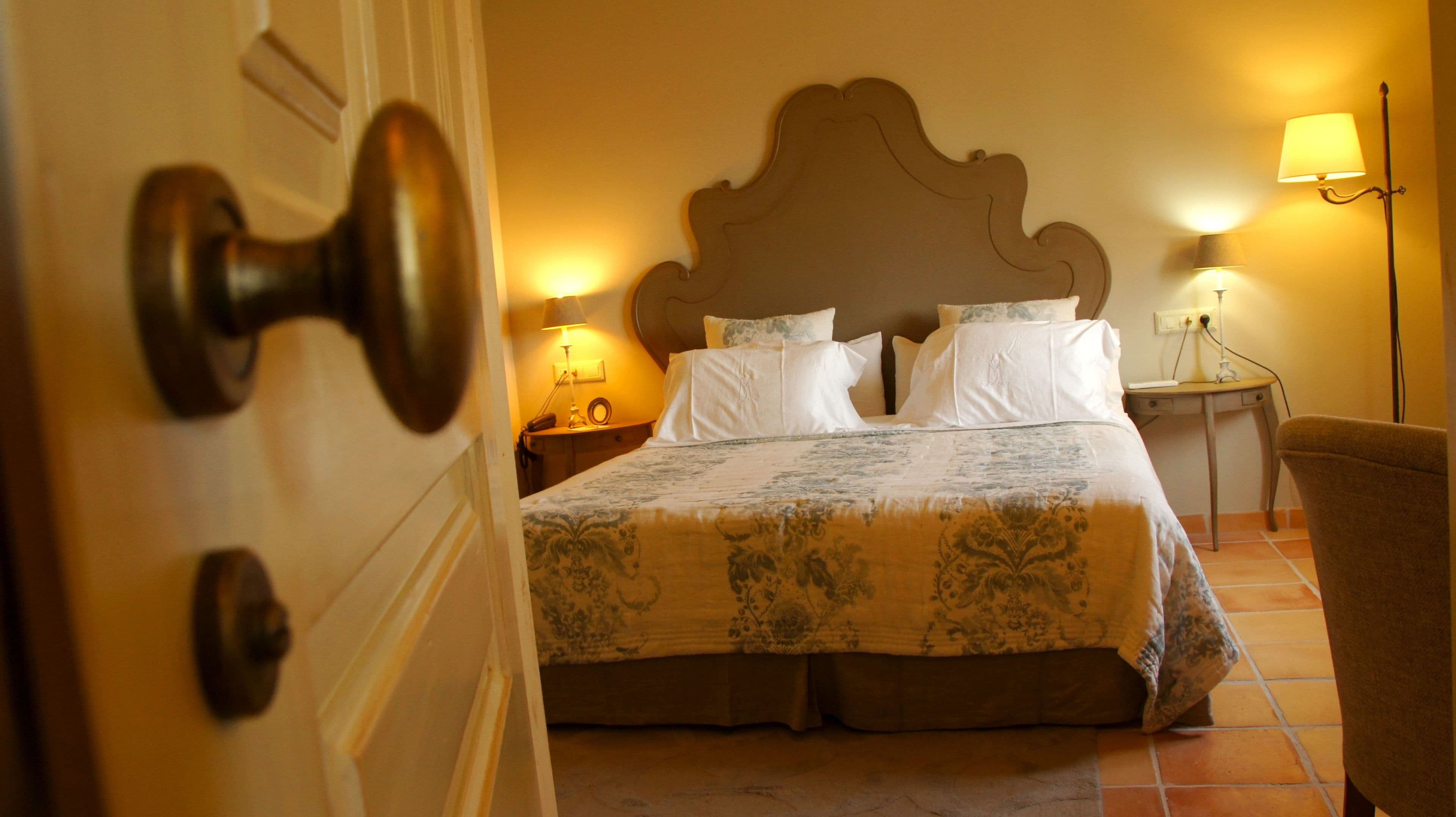 A hotel room with a large bed, a nightstand, a chair, and a lamp.