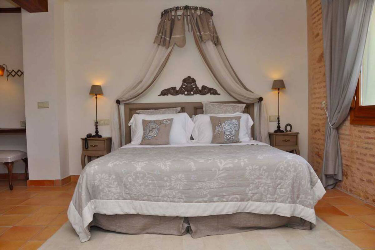 A bedroom with a large bed, two bedside tables, a chair, and a canopy bed.