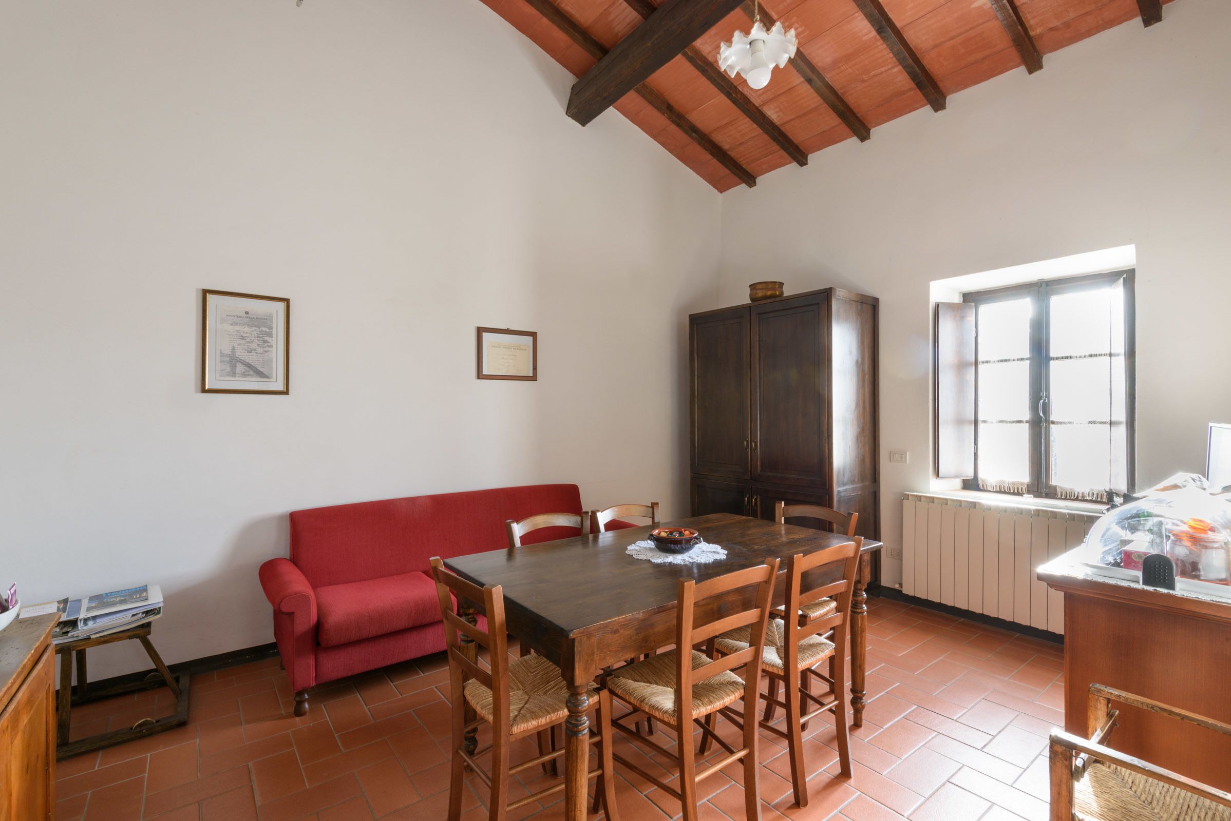A dining area with a wooden table and chairs, a red sofa, and a cabinet.