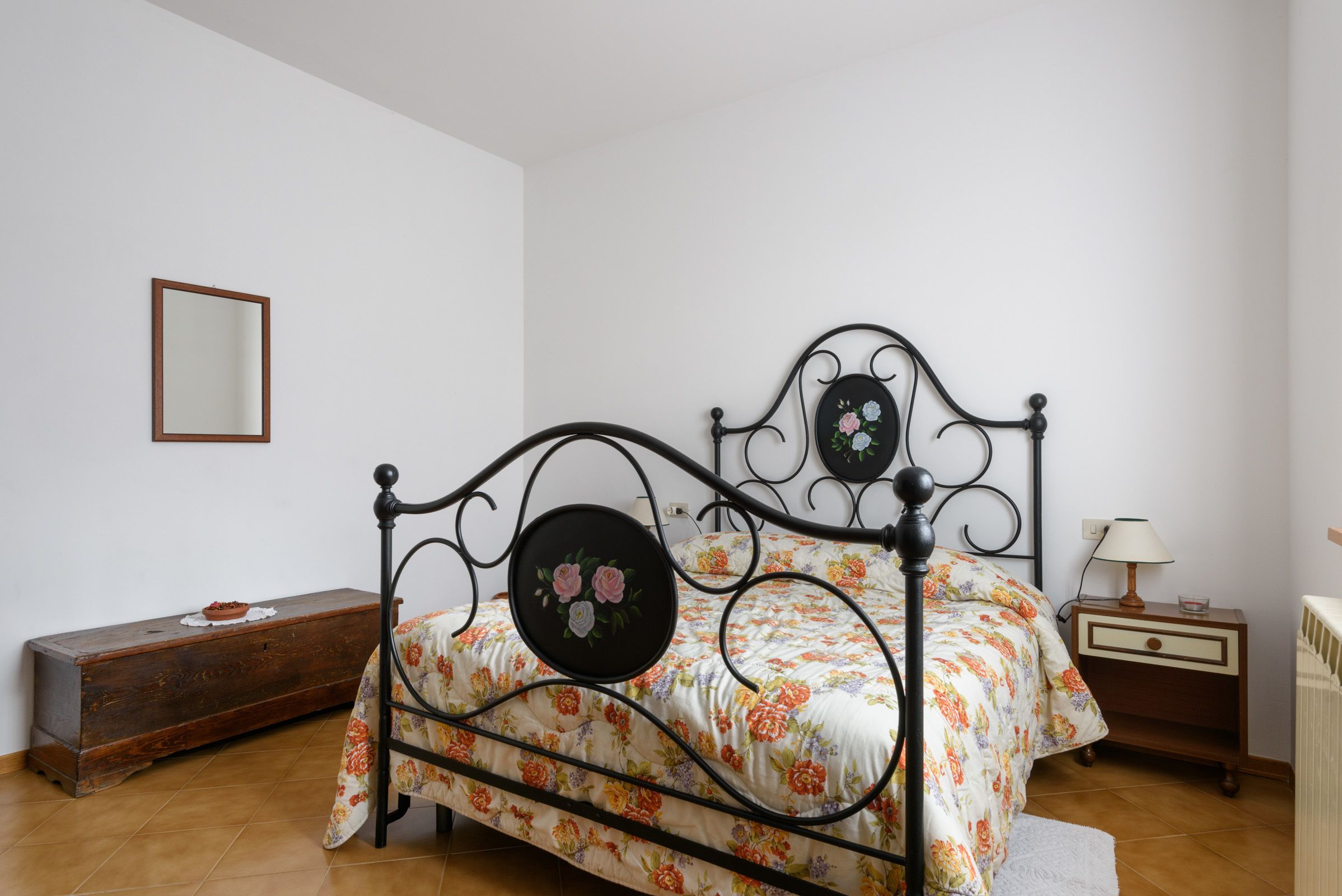 Ein Bett mit floralem Überwurf und einem runden Spiegel am Kopfteil.