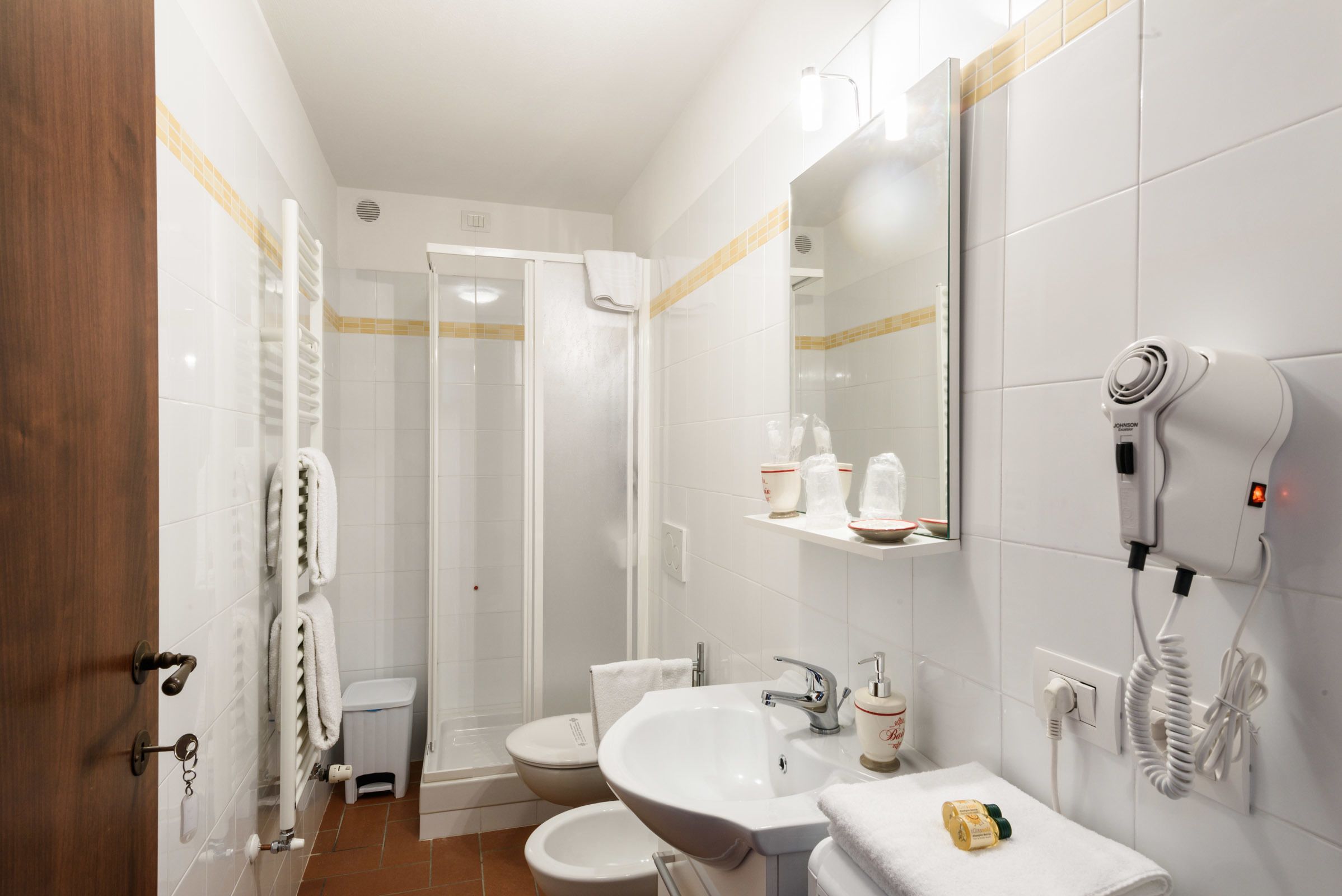 Un bagno con doccia, toilette, lavandino e asciugacapelli a parete.