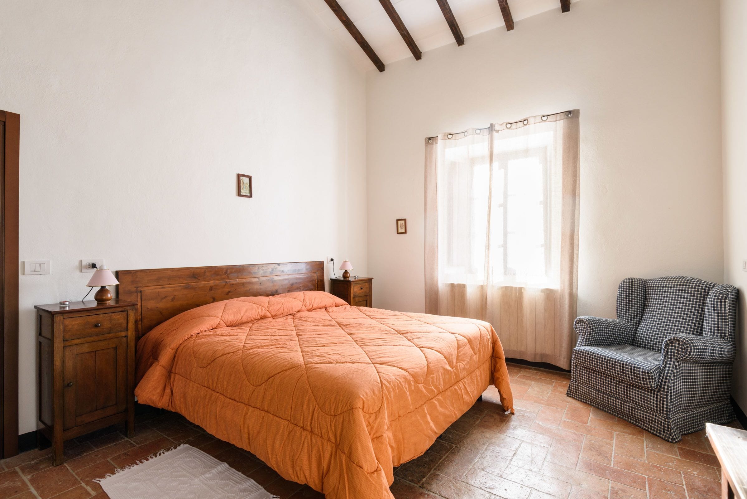 Une chambre à coucher avec un lit en bois, une table de chevet, une chaise et une fenêtre avec des rideaux.