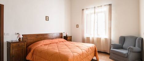 A bedroom with a wooden bed, a nightstand, a chair, and a window with curtains.