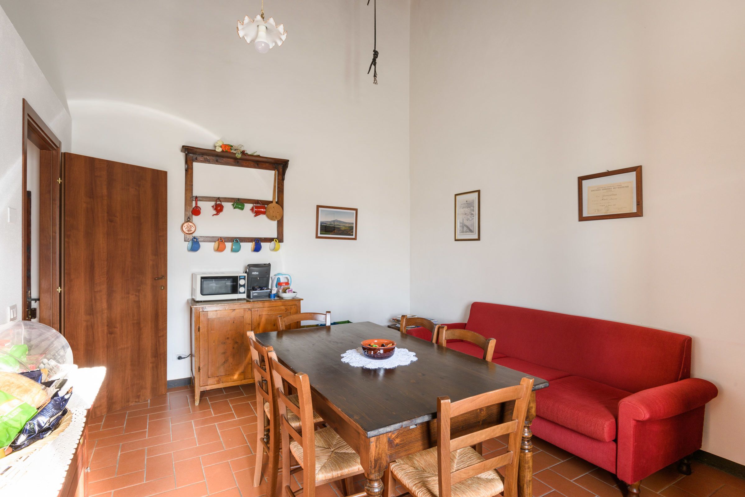 A dining area with a wooden table, chairs, a red sofa, a microwave, and a small cabinet.