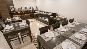A dining area with multiple tables set for service, equipped with white tableware and a buffet line in the background. - Dweik Hotel 2 (Aqaba)