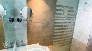 A bathroom with a marble sink, two round mirrors, and a glass shower enclosure.