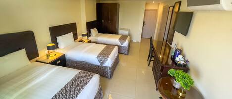 A hotel room with two beds, a desk, a chair, a TV, and a potted plant.