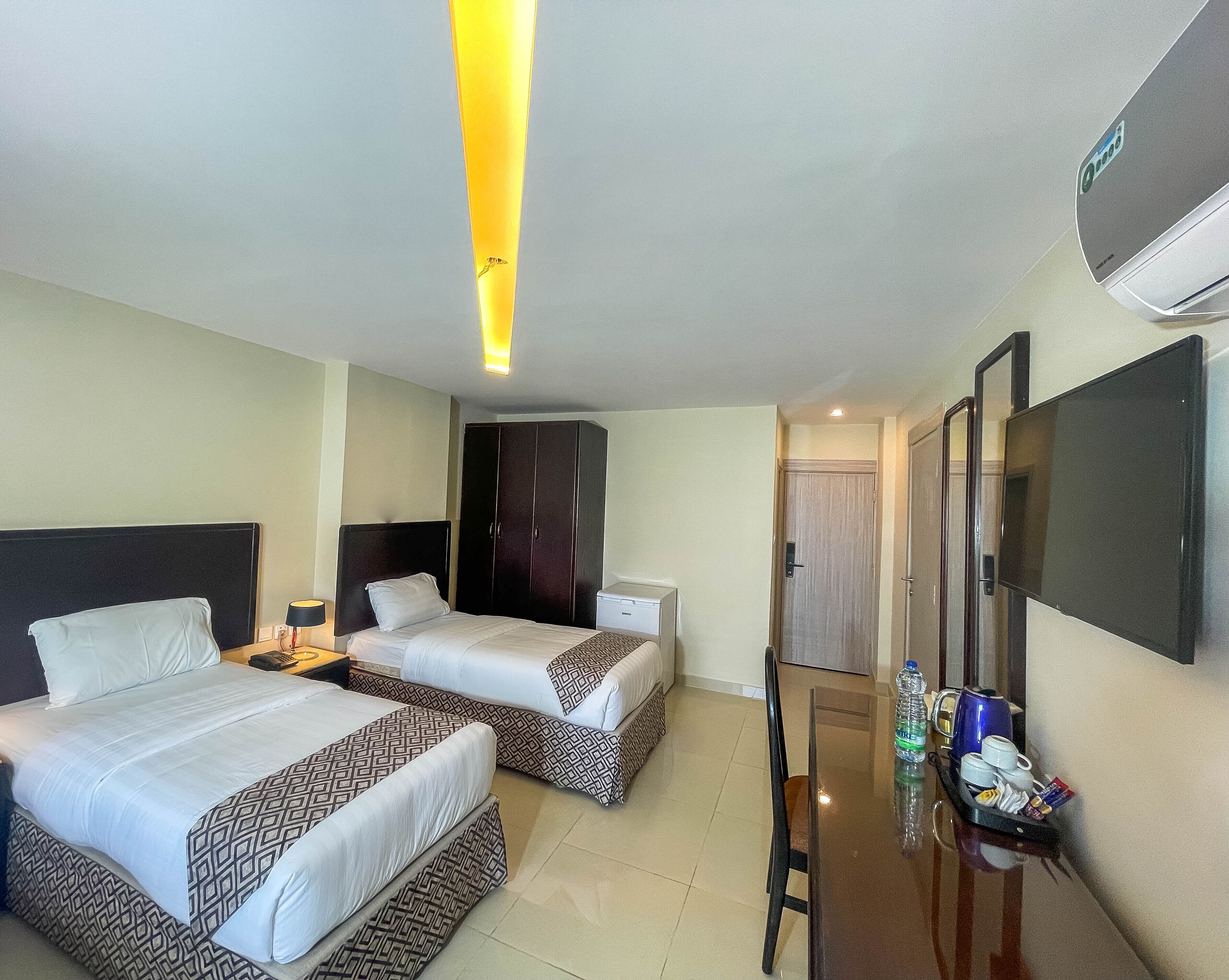 A hotel room with two beds, a desk, a wardrobe, and a TV.