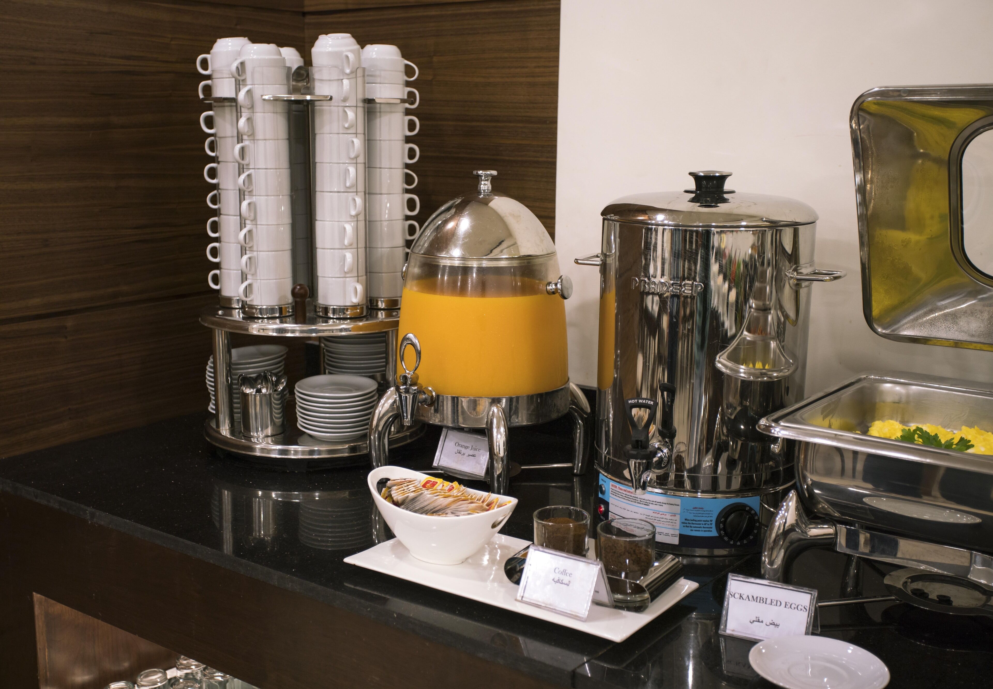 A buffet setup with coffee, scrambled eggs, and a hot water dispenser.